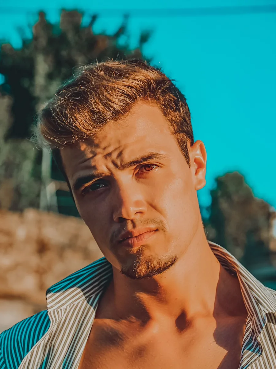 Original photo — a man with light hair in an open striped shirt against a bright turquoise wall