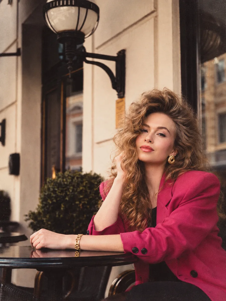 80s Filter result — the same woman in a bright magenta padded-shoulder blazer with big 1980s hair, seated by a street lamp