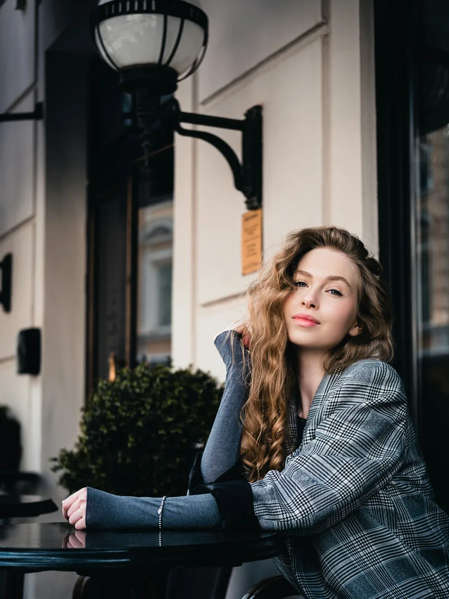 Original photo — a woman in a grey checked blazer leaning against a wall by a lamp