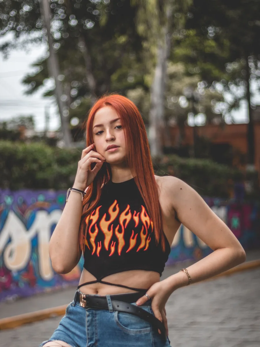 Original photo — a woman with red hair in a black flame-print top against a graffiti wall