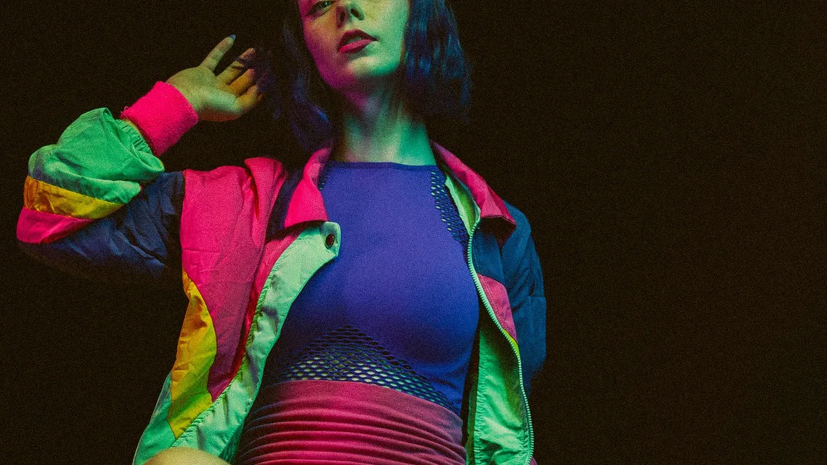 A woman sitting in a chair with bold 1980s studio fashion and lighting
