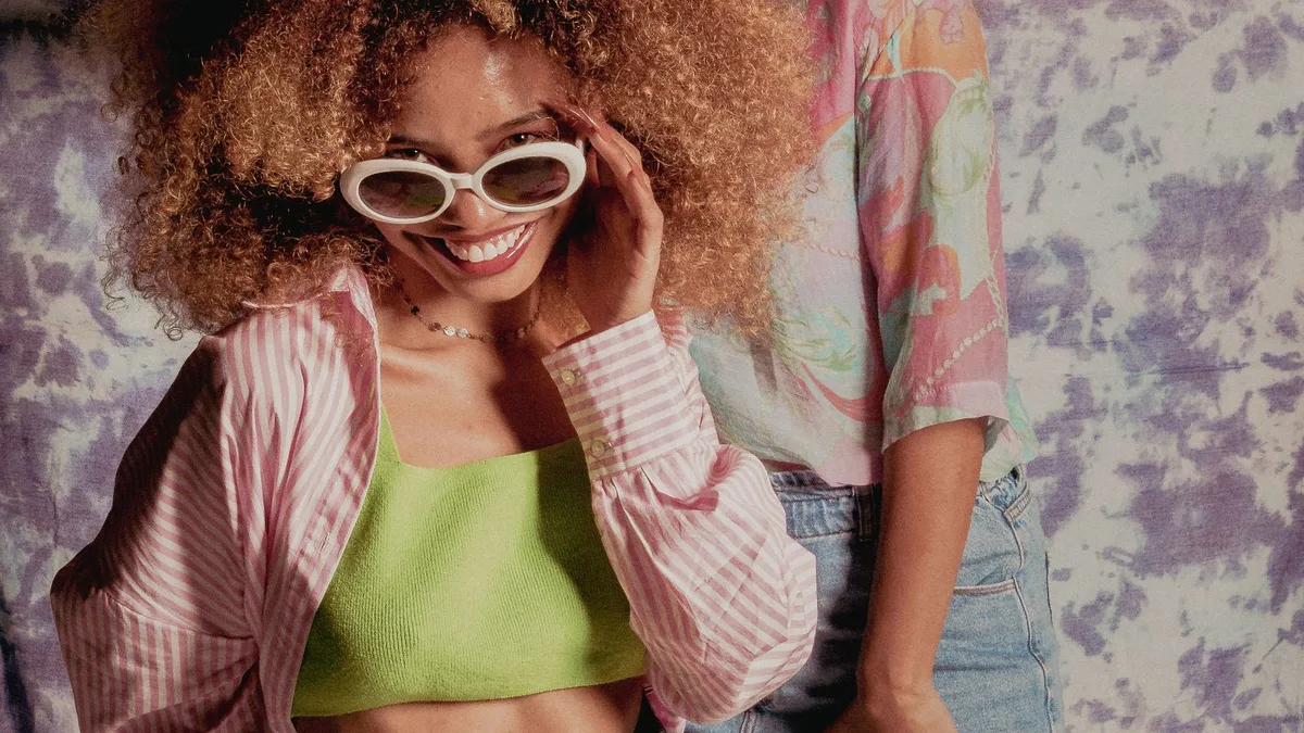 Two women in colourful vintage-inspired outfits and sunglasses posing together