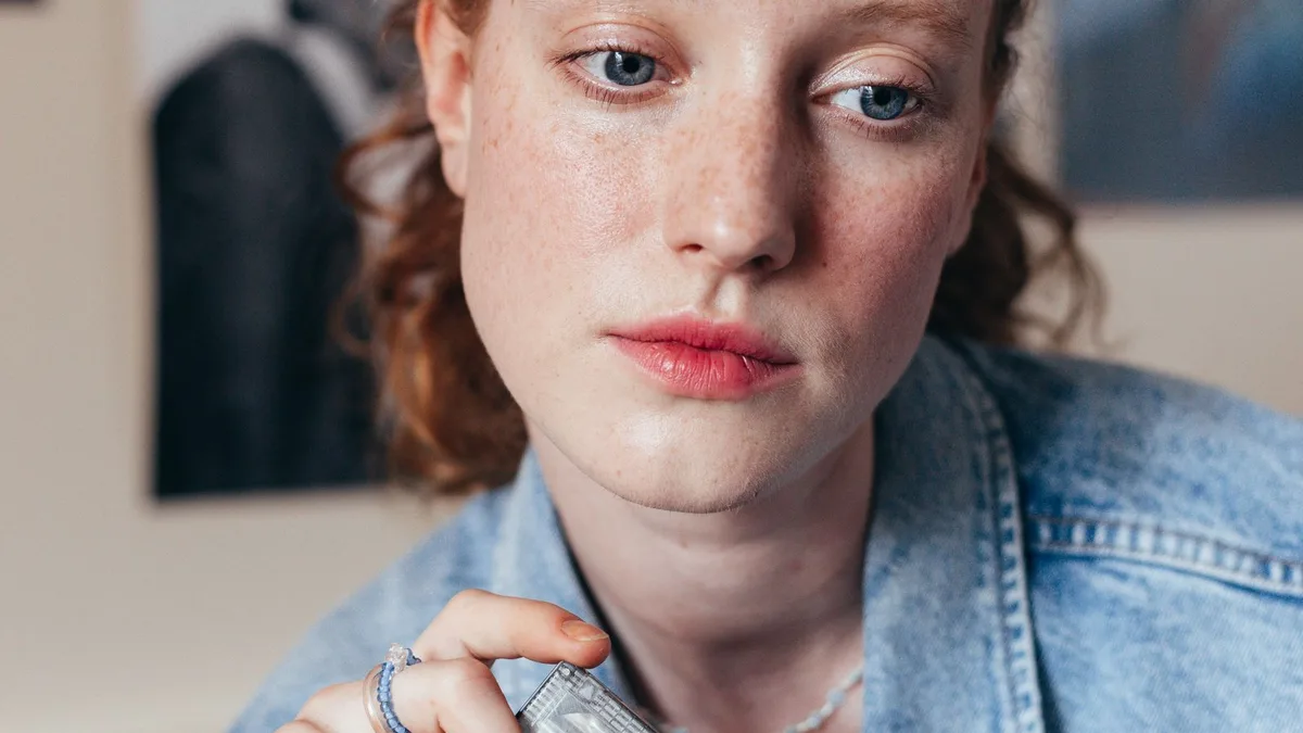 A young woman holding a cassette tape in a denim jacket, 80s-styled photo