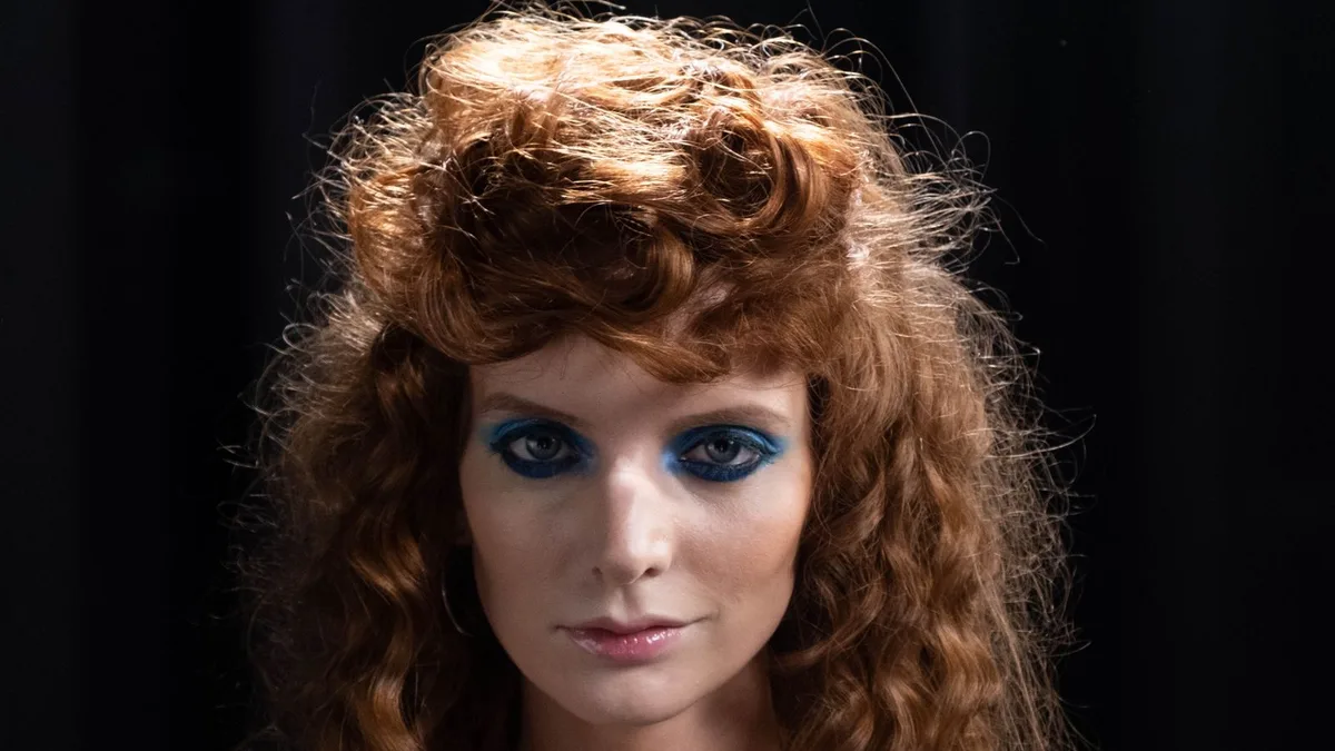A young woman with bold blue eyeshadow under disco-ball lighting