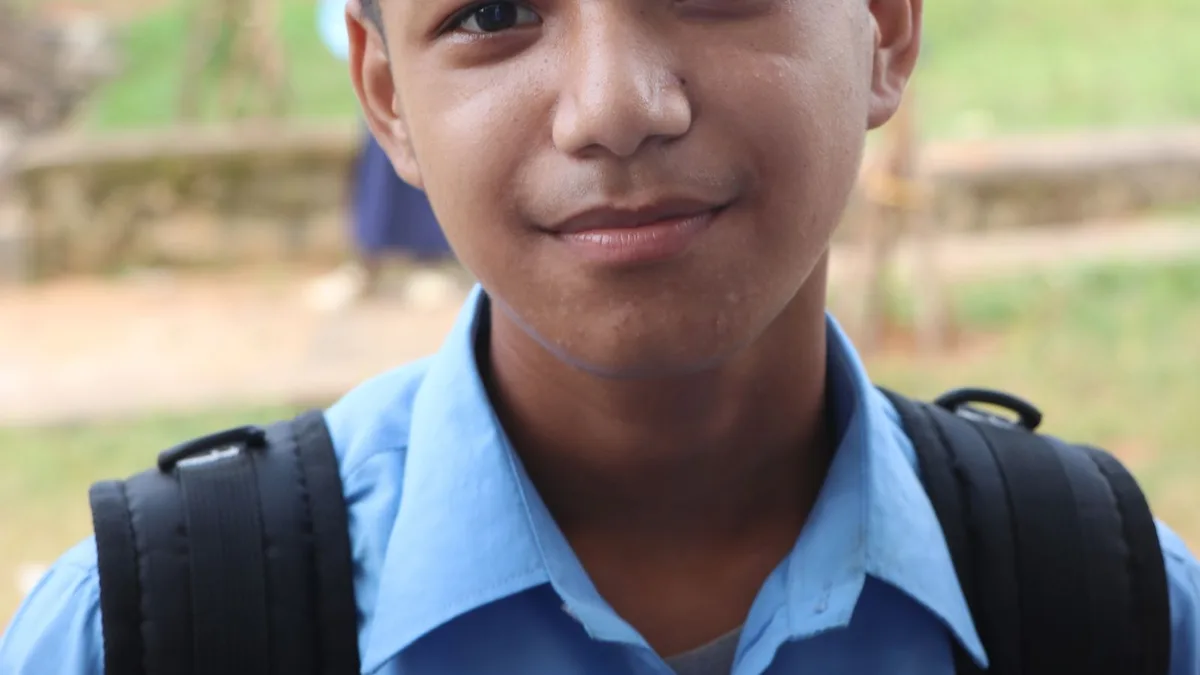 A teenage boy in a school uniform smiling outdoors