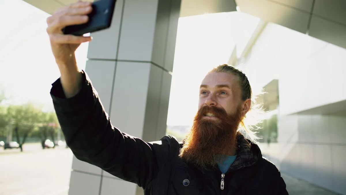 A bearded man taking a selfie outdoors in bright sunlight