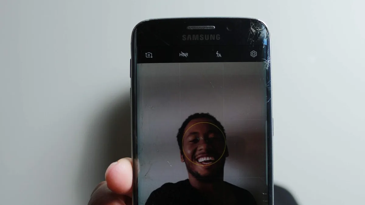A man holding an iPhone with the screen reflecting light, indoors