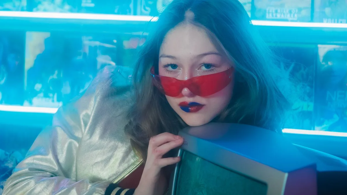 A woman posing in a retro-styled room with a vintage television and neon lighting