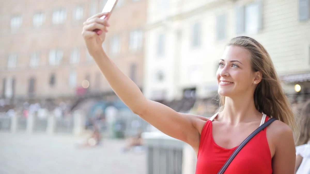 A woman taking a smiling selfie outdoors in daylight
