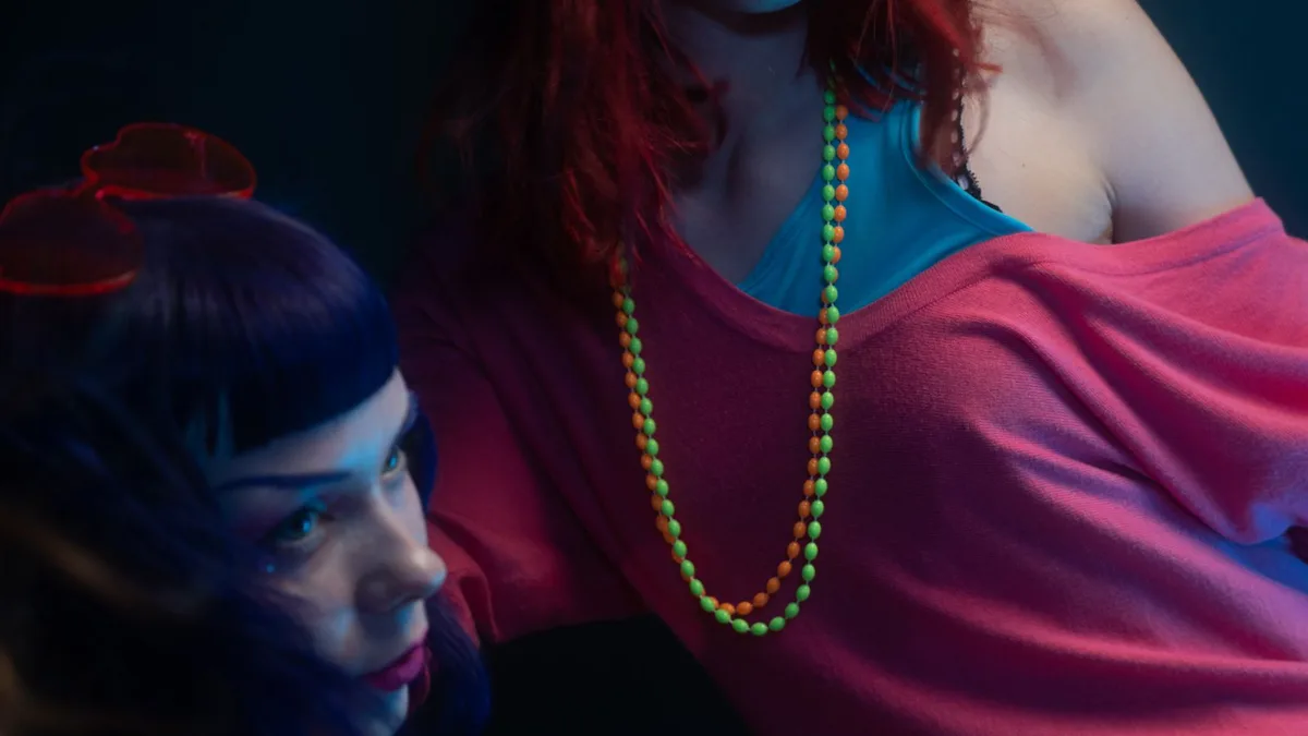 Two women in colourful bold 1980s fashion under vibrant lighting