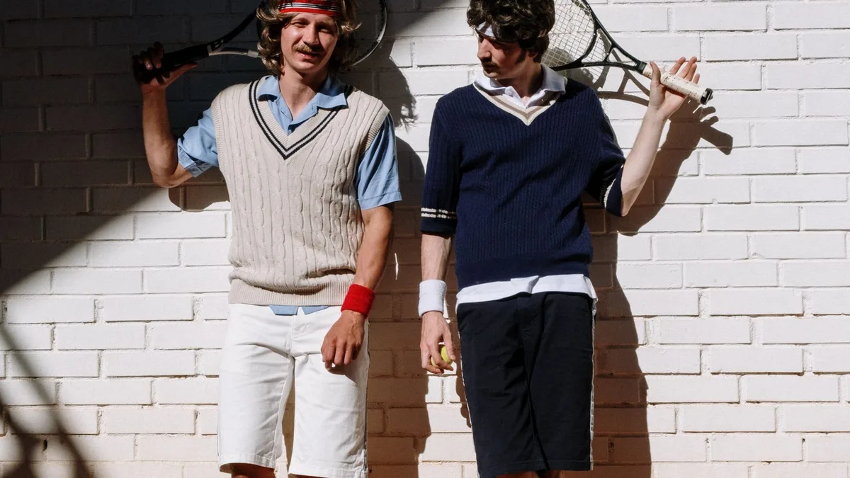Two people in vintage sportswear holding tennis rackets in a retro style
