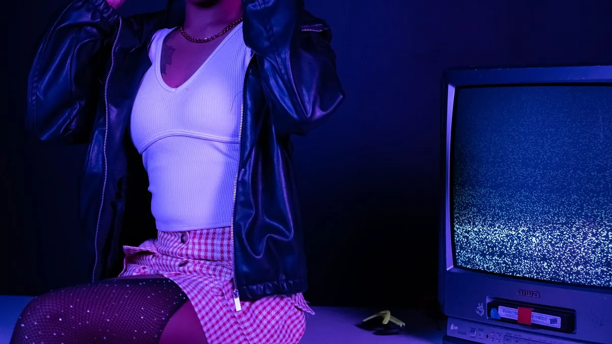 A person in a leather jacket beside a static-filled vintage TV under blue neon