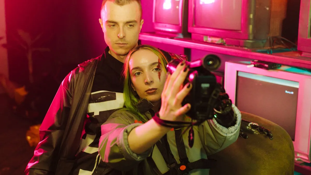 A couple with a retro camcorder among CRT televisions under pink neon